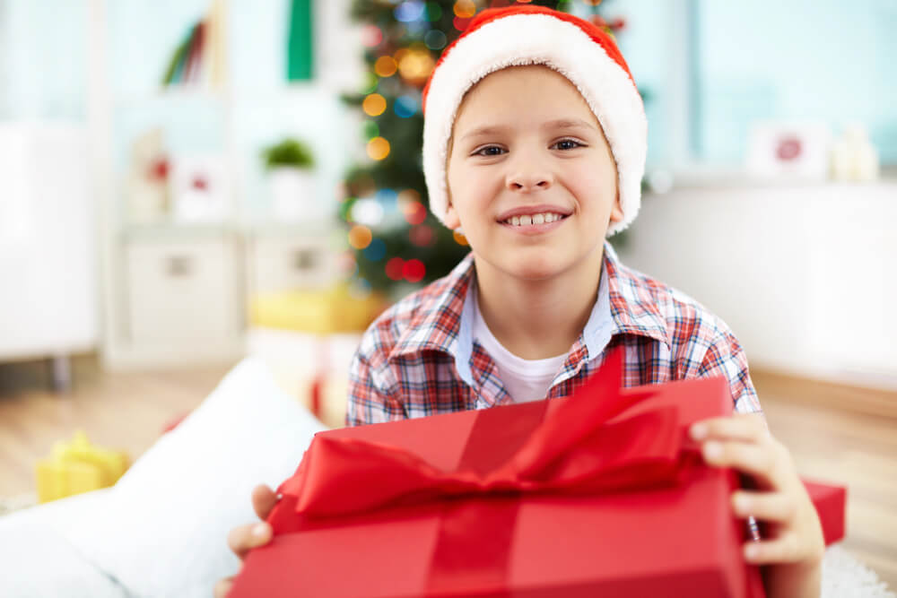 A boy with a Santa hat holding a gift. Pick from these 11 easy ways to get free toys for kids.