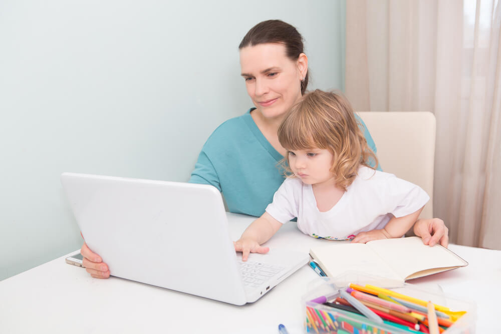 A mom and her son looking at a laptop. Here are 12 ways single moms can build wealth in 2024.