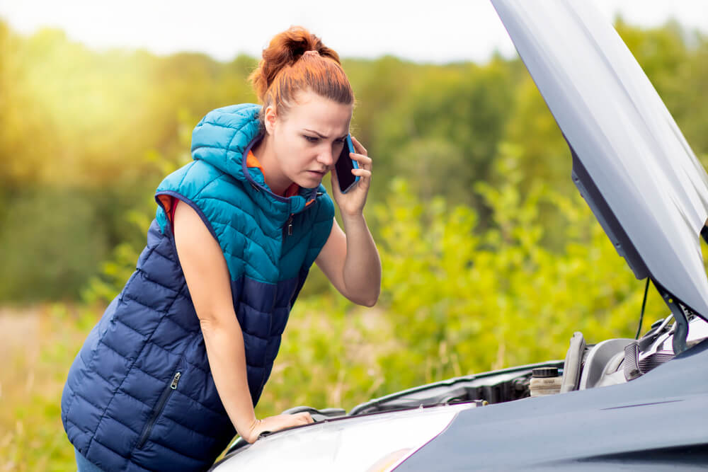 A woman on the phone and looking at the hood of her car. Check here for 12 ways single moms can build wealth in 2024.