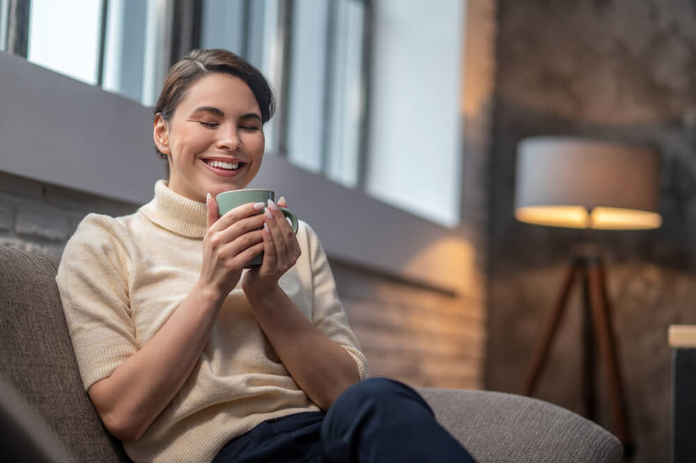 A woman happily holding a mug. Check out these 12 ways single moms can build wealth in 2024.