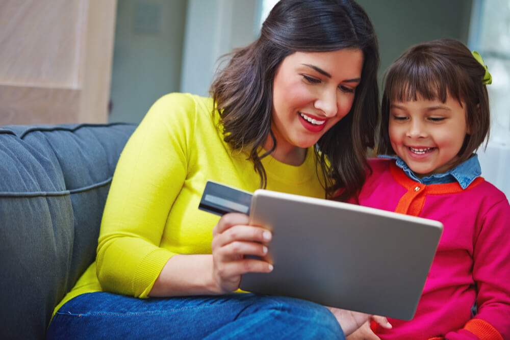 A woman and a child looking at a tablet. The mom is holding a card. Here are 12 ways single moms can build wealth in 2024 you can check.