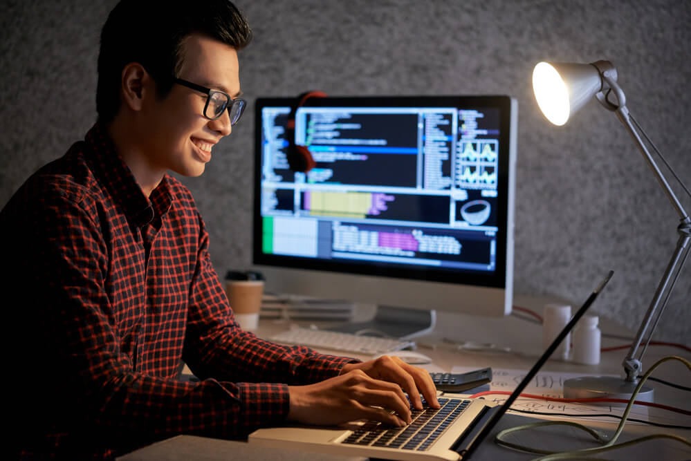 A bespectacled man working in front of a laptop and another monitor. Read about these 22 high-paying jobs without a degree to pursue in 2024.