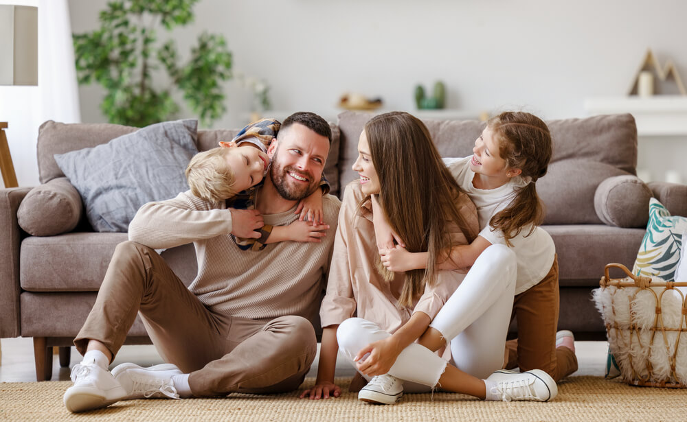 A couple sitting on the floor, each one with a kid embracing them from the back. You can read here these 31 co-parenting tips to make shared custody a success.
