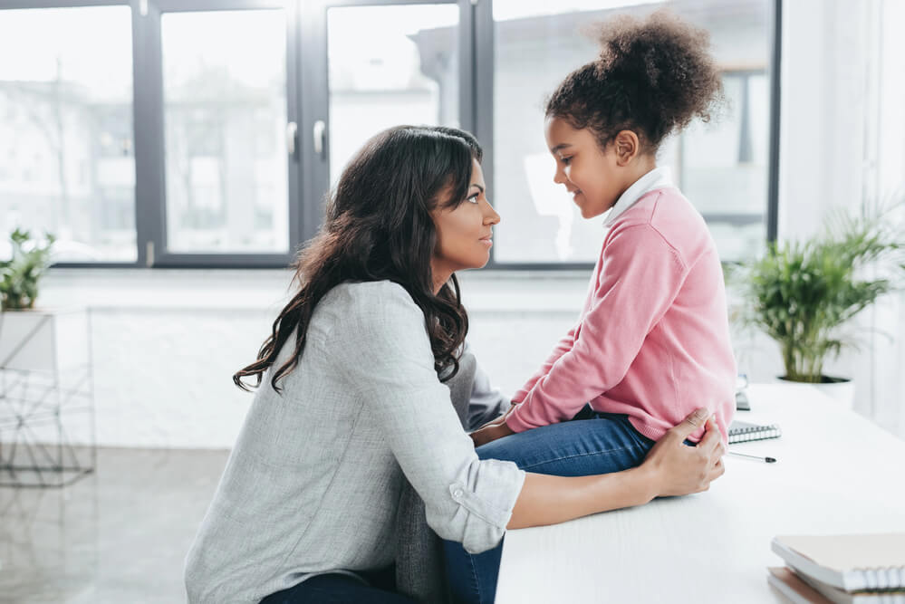 A woman talking to her child who's sitting on a kitchen counter. Check out these 31 co-parenting tips to make shared custody a success.