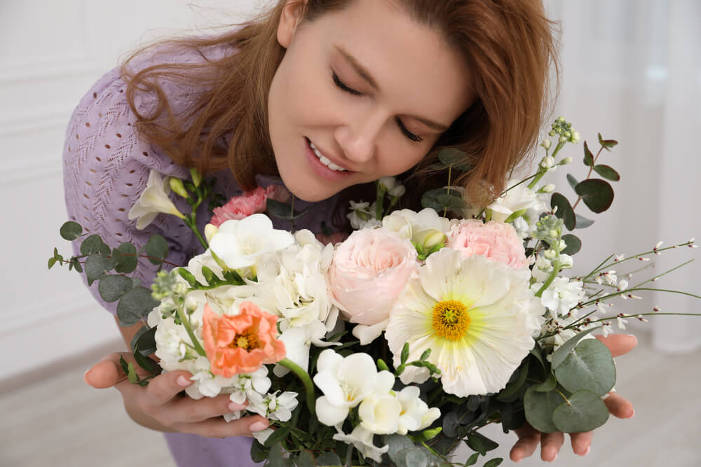 A smiling woman with flowers. Here are 32 best gifts for single moms to check out.