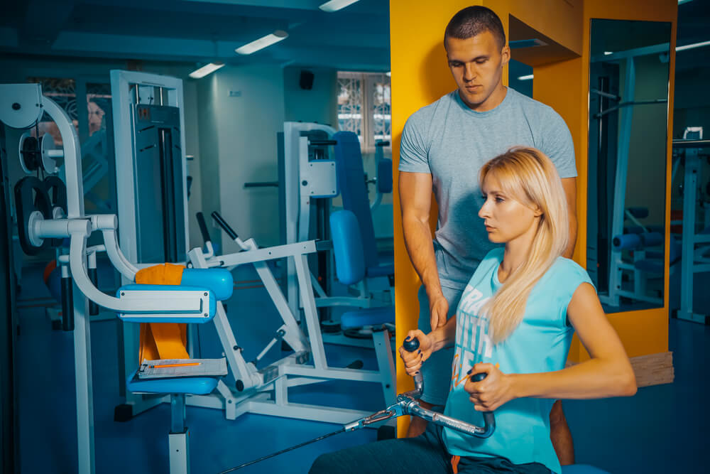 A woman using a gym equipment with a man beside her. Check out 32 best gifts for single moms here.