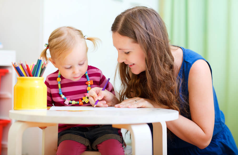A woman teaching a child how to write. Check out these 6 places to find a babysitter in 2024.