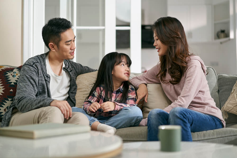A man and a woman talking to child while seated on a sofa. Learn more about these 7 benefits of parenting classes and where to find them.