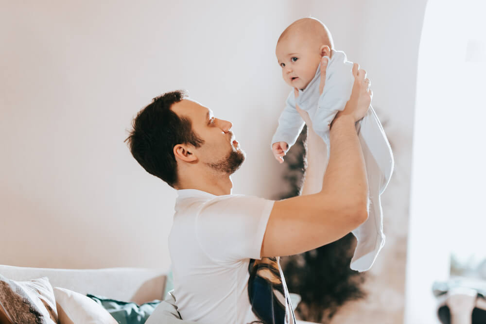 A man lifting a baby in the air. Check out these 7 things you need to know before dating a man with kids in 2024.
