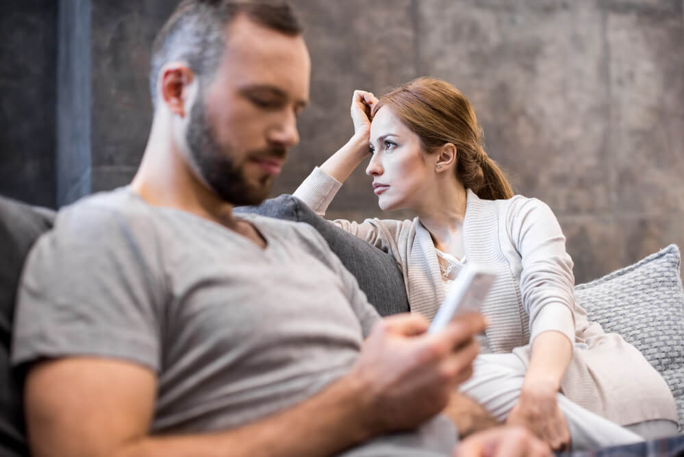 A man texting beside a woman who is looking far and ignoring him. Check out these 7 things you need to know before dating a man with kids in 2024.