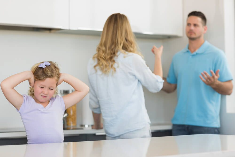 A couple arguing while a child tries to cover her ears. Find out more about these 7 things you need to know before dating a man with kids in 2024.