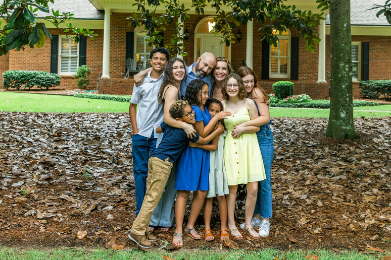 A large blended family embraces in front of their house.