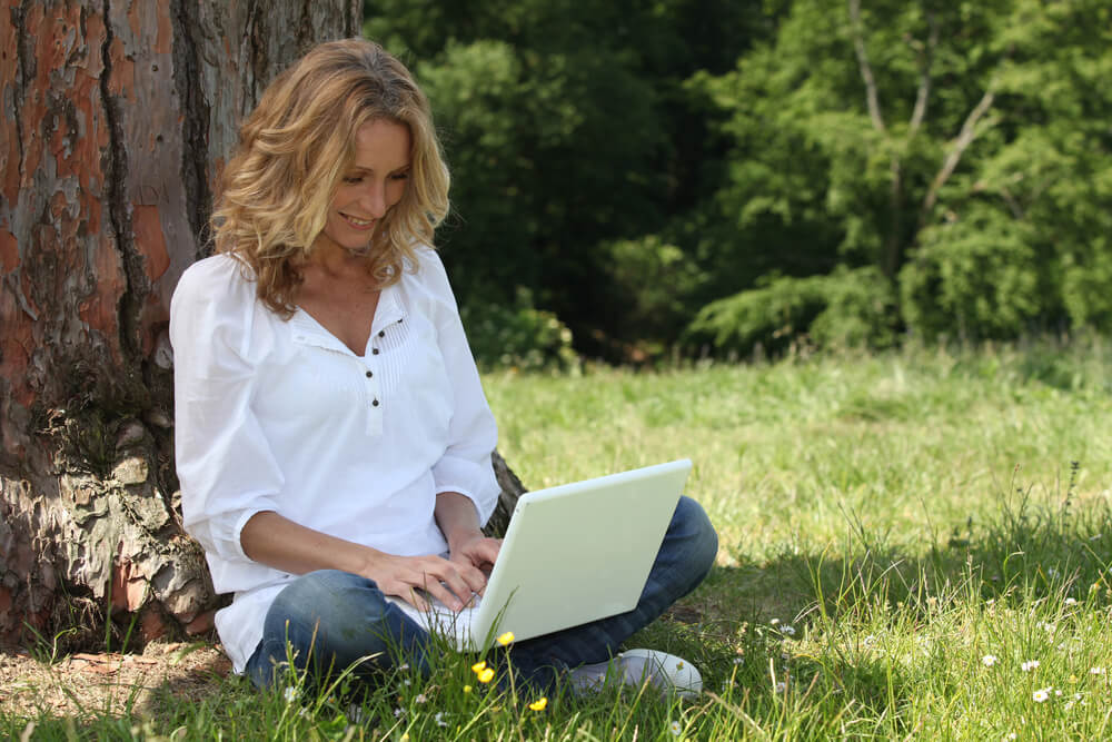 A woman happily scrolls the internet with her laptop. There are many articles to choose from if you're a Catholic looking for dating sites.