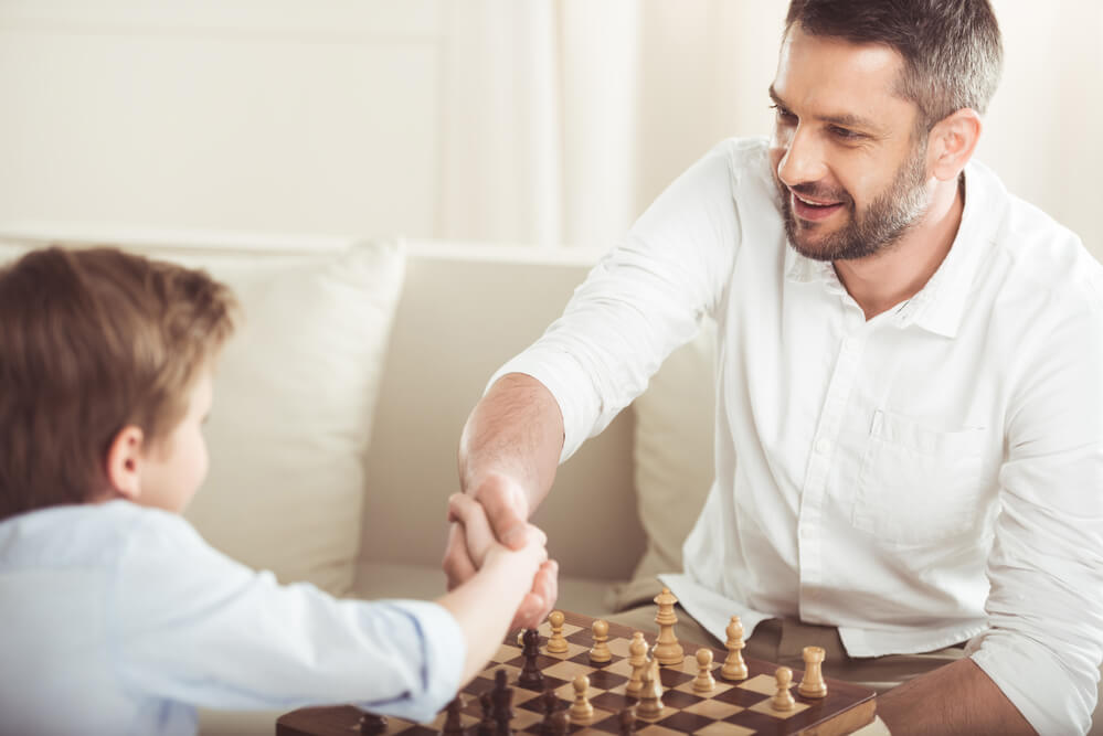 A father and son happily playing chess. Learn about dating someone with kids.