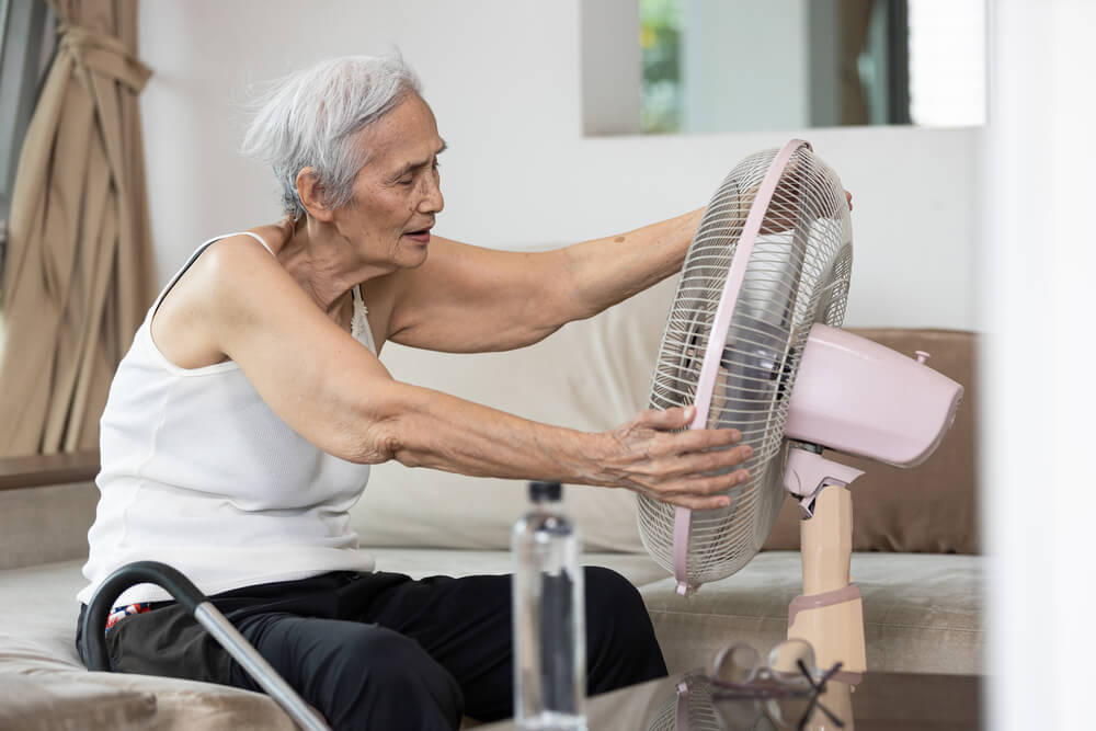 Elderly woman tries to cool off in the heat. Learn how you can qualify for a free air conditioner.