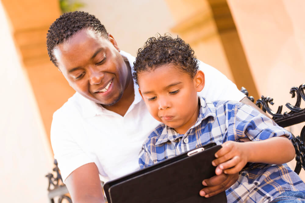 The dad smiles as the son watches something on the tablet. You can buy your kids a tablet if you’re eligible for ACP because you can get a one-time discount of up to $100.
