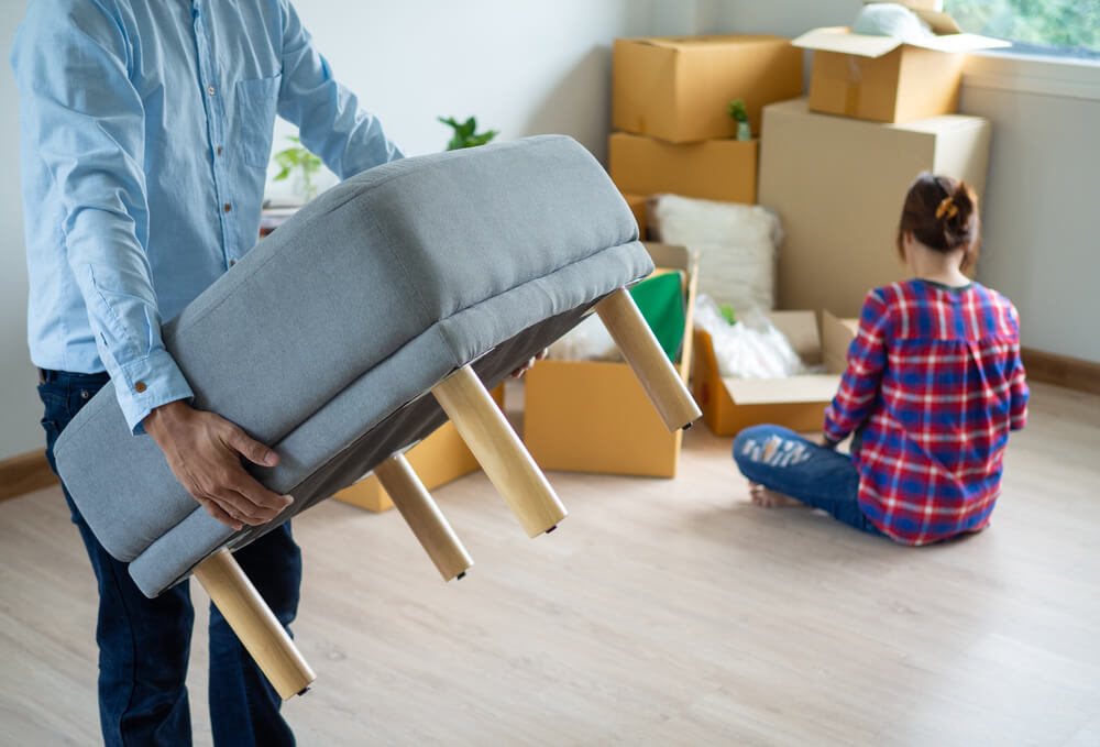 The man is carrying a chair and the woman is packing the box. Small furniture in good condition like office chairs, nightstands, and side tables can be donated to Pickup Please.