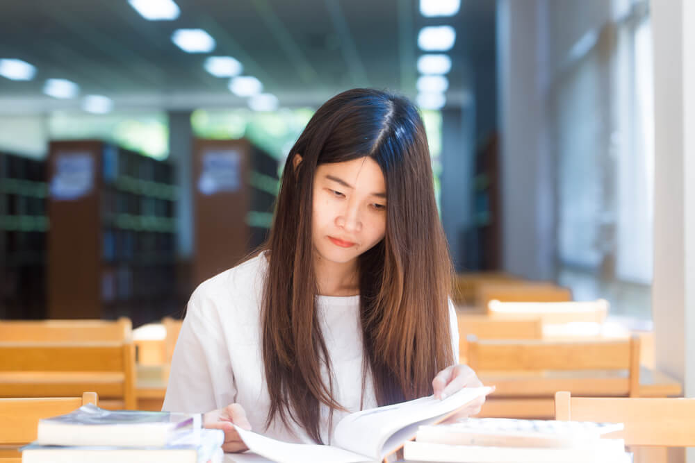 A young Asian woman in a library. This is how to get free wifi away from home.