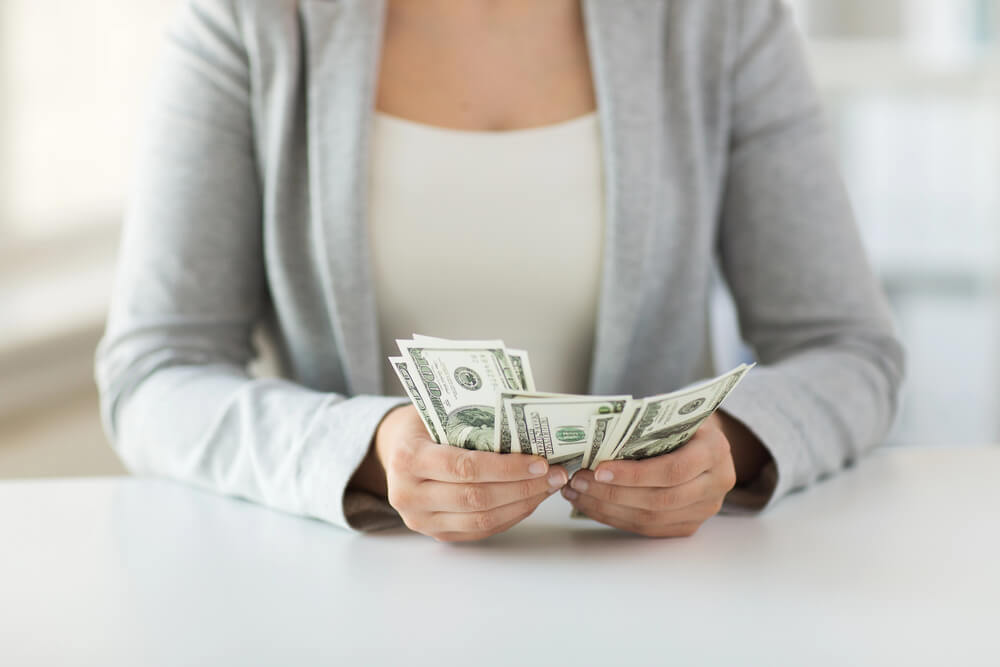 The woman counts the money she's holding. To eliminate debt, choose a method to pay off debt.