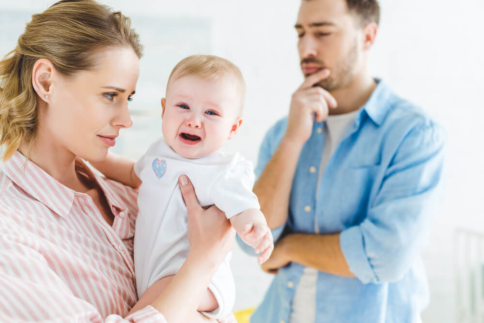 A mom holding a crying baby while the dad is getting annoyed. Blending families? How to make a blended family work is resolved here.