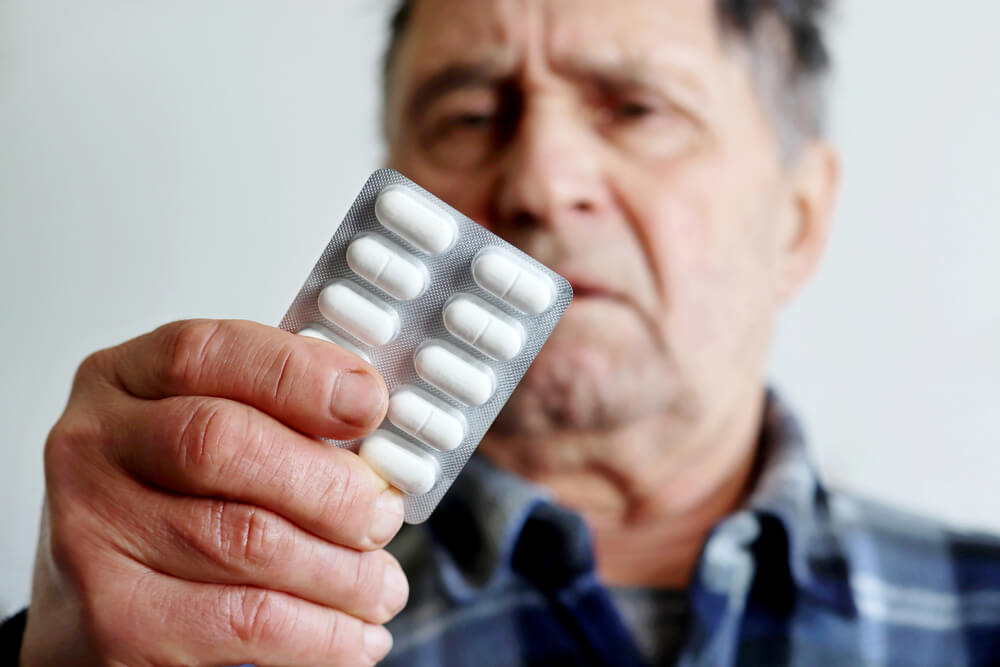 The elderly man holds white pills. Publix offers a decent list of affordable medications.