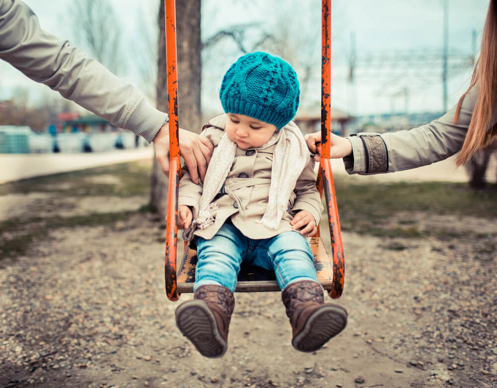 A child is pulled between two parents on a swing. Beware of these 18 sneaky divorce tactics so you can overcome them.