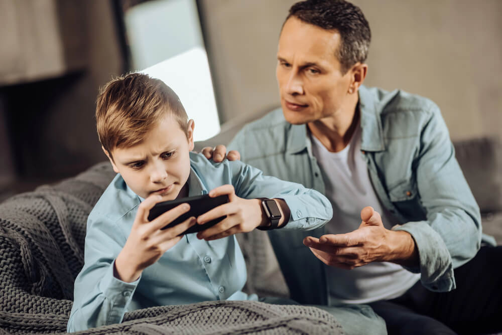 A man prohibiting a child from using a mobile phone. What is parental alienation? Recognize the 18 signs here.