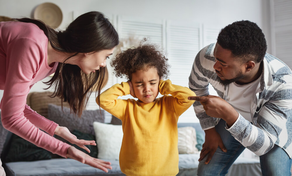 A husband and wife reprimanding their child who is covering his ears. What is parental alienation? Recognize the 18 signs you have to know.